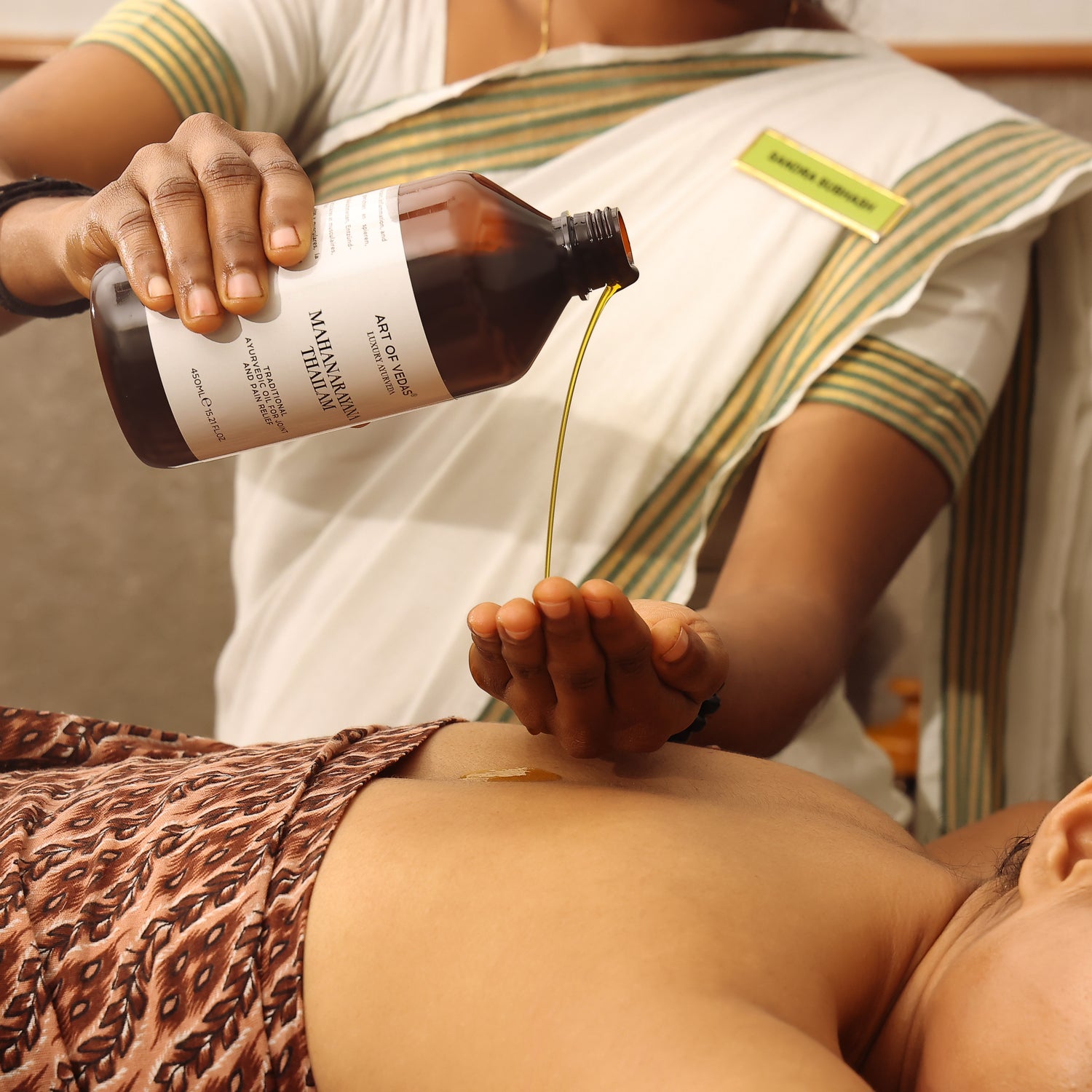 Ayurvedic practitioner pouring Art of Vedas Thailam oil during traditional Abhyanga massage treatment